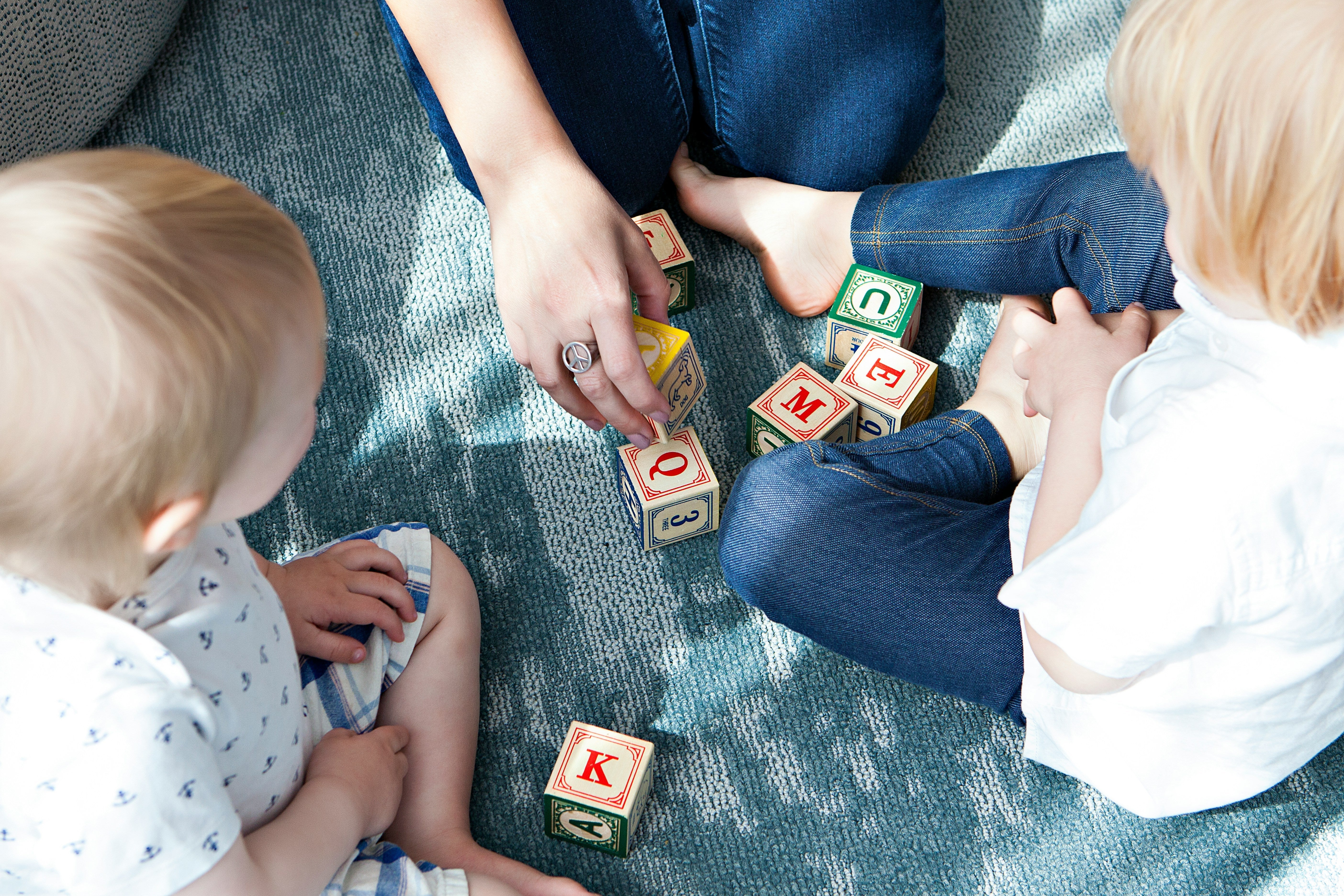 Baby girl playing with wooden alphabet blocks on soft carpet, educational toddler toy gift idea.