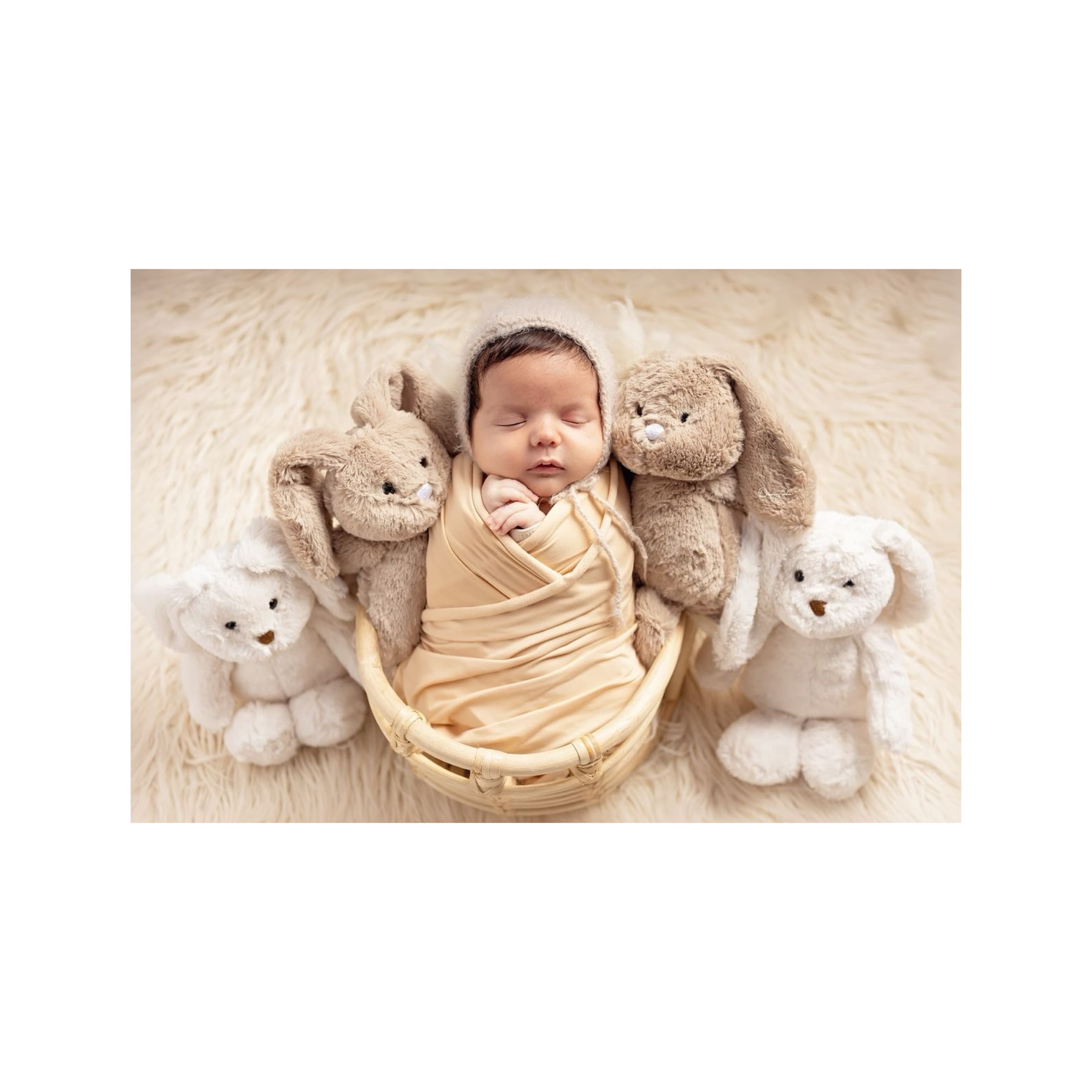 Newborn baby wrapped in beige swaddle blanket lying on soft bed surrounded by plush teddy bears, perfect for gender reveal party gift set or baby shower present idea.