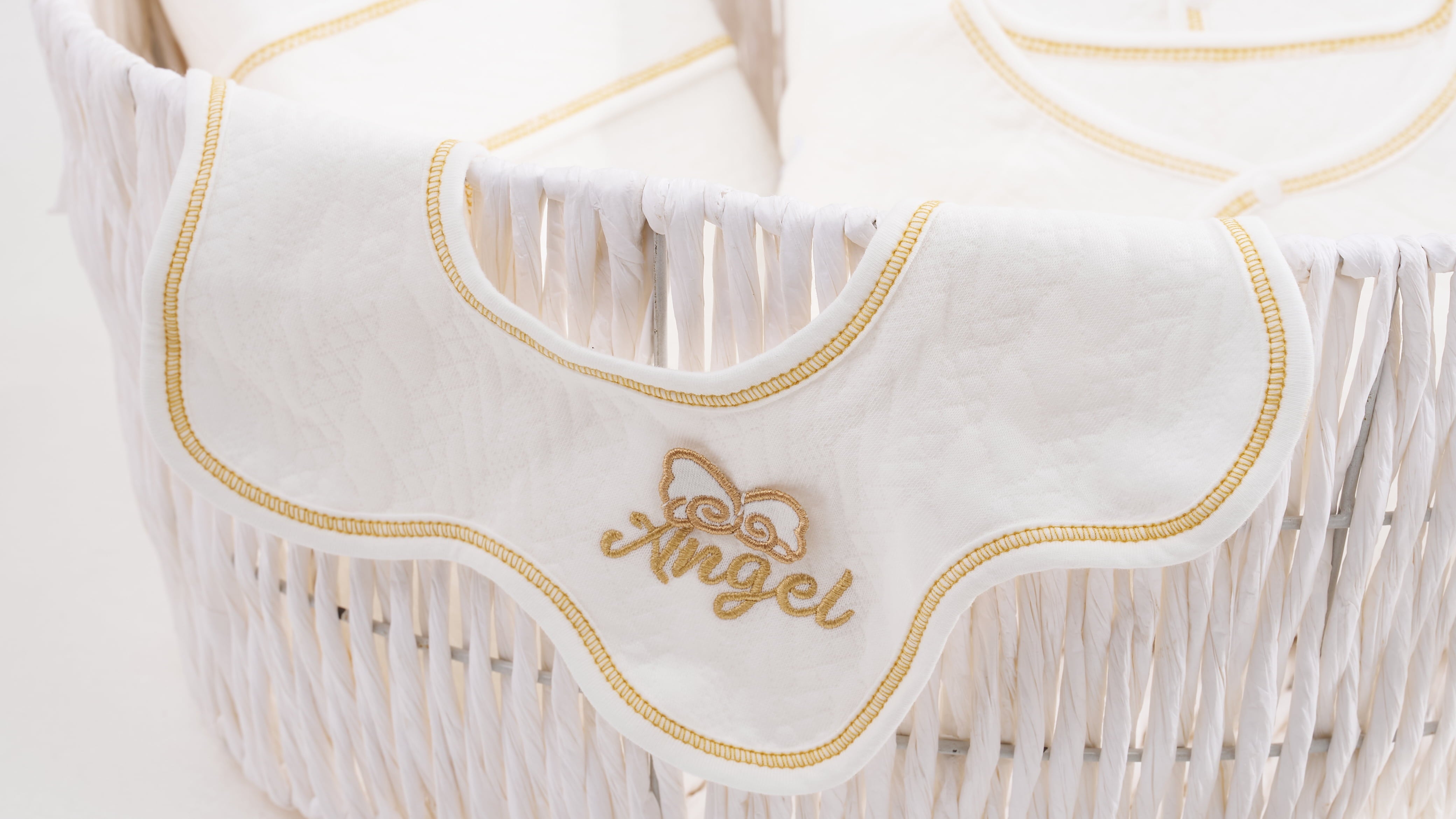 Close-up of a white baby bib with gold embroidery reading “Angel,” ideal for a baby gift set.
