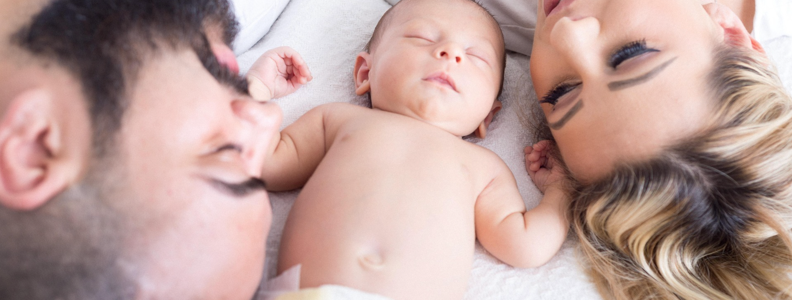New mum and dad sleeping in bed with newborn baby during postpartum recovery