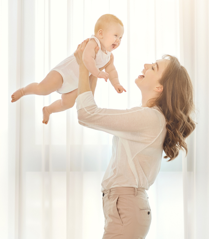 Mother joyfully holding her baby up, both wearing cozy pieces from a Babywonders gift set — a heartwarming moment of love and comfort.