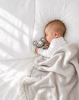 Sleeping newborn baby wrapped in a soft tassel blanket and cuddling a crochet elephant rattle, a thoughtful baby shower gift and newborn essential in the UK.