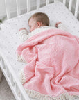 Sleeping newborn baby covered with a pink cotton baby blanket in a cot, soft breathable blanket for nursery and everyday comfort.