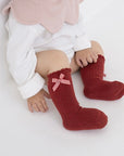 Infant sitting wearing red socks with cute checkered bow, holiday style baby outfit.