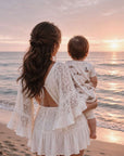 Mother holding baby wearing beach print zip swim romper by the seaside at sunset in soft coastal lifestyle setting