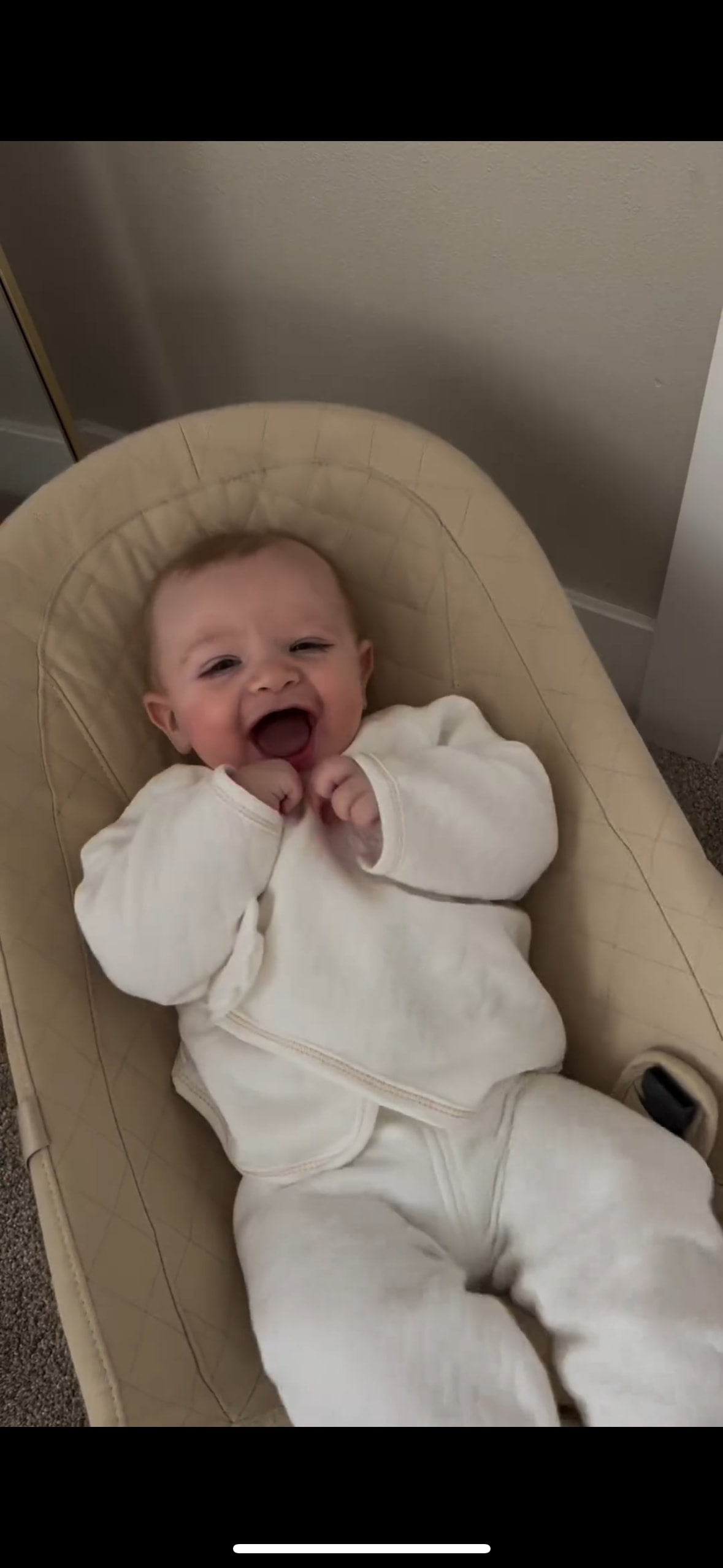 Smiling baby wearing a white Babywonders UK outfit in a cozy baby seat – customer photo