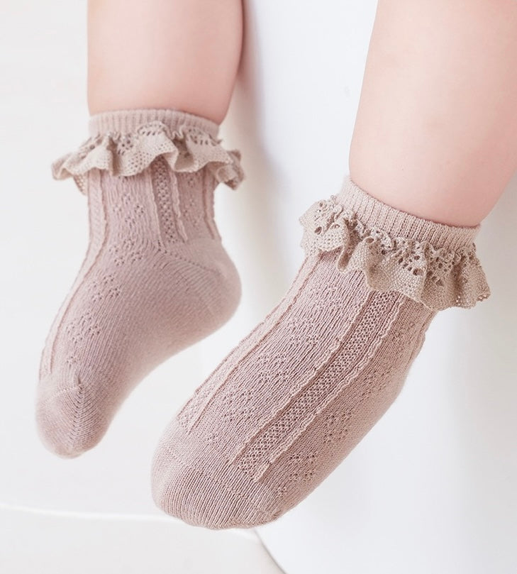 Baby wearing beige lace frill socks, cozy cotton knit with elegant ruffled trim.