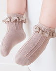 Baby wearing beige lace frill socks, cozy cotton knit with elegant ruffled trim.