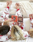 Family in matching Christmas pajamas reading holiday books on couch, cozy festive atmosphere.