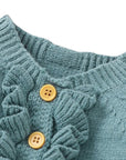 Close-up of ribbed neckline and wooden button details on blue-green knitted baby romper showing fine craftsmanship.