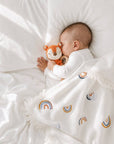 Sleeping newborn baby cuddling a crochet fox rattle under a tassel rainbow blanket, a thoughtful baby shower gift and newborn essential in the UK.