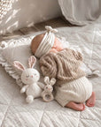 Newborn baby resting beside a handcrafted crochet rabbit comfort toy and matching bunny rattle, a thoughtful baby shower gift and nursery essential for sensory play.
