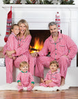Family wearing matching red striped Christmas pajamas sitting by fireplace