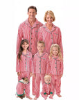 Family in matching red and white striped Christmas pajamas with kids, baby, and dog