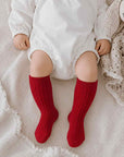 Baby wearing red fluffy fleece knit knee-high socks on soft neutral blanket