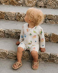 toddler wearing dinosaur print rash guard swimsuit sitting on stone steps UV protection swimwear