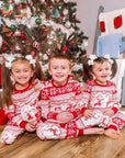 Children wearing red reindeer Christmas matching pajamas by the tree, cozy holiday loungewear
