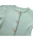 Close-up of wooden button detail on light green ribbed cotton baby jumpsuit.