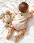 Baby wearing neutral linen romper with floral ruffle knit socks in khaki