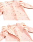 Close-up of ruffled shoulder design and button front on pink cotton knit baby romper.