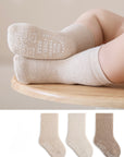 Beige socks with text worn by a child on a wooden stool, with additional pairs displayed below.