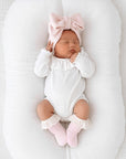 Newborn baby girl wearing a white ruffle collar baby bodysuit with eyelet lace cotton baby socks in soft minimalist nursery setting