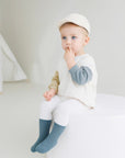Toddler boy sitting in white outfit wearing blue ribbed cotton socks