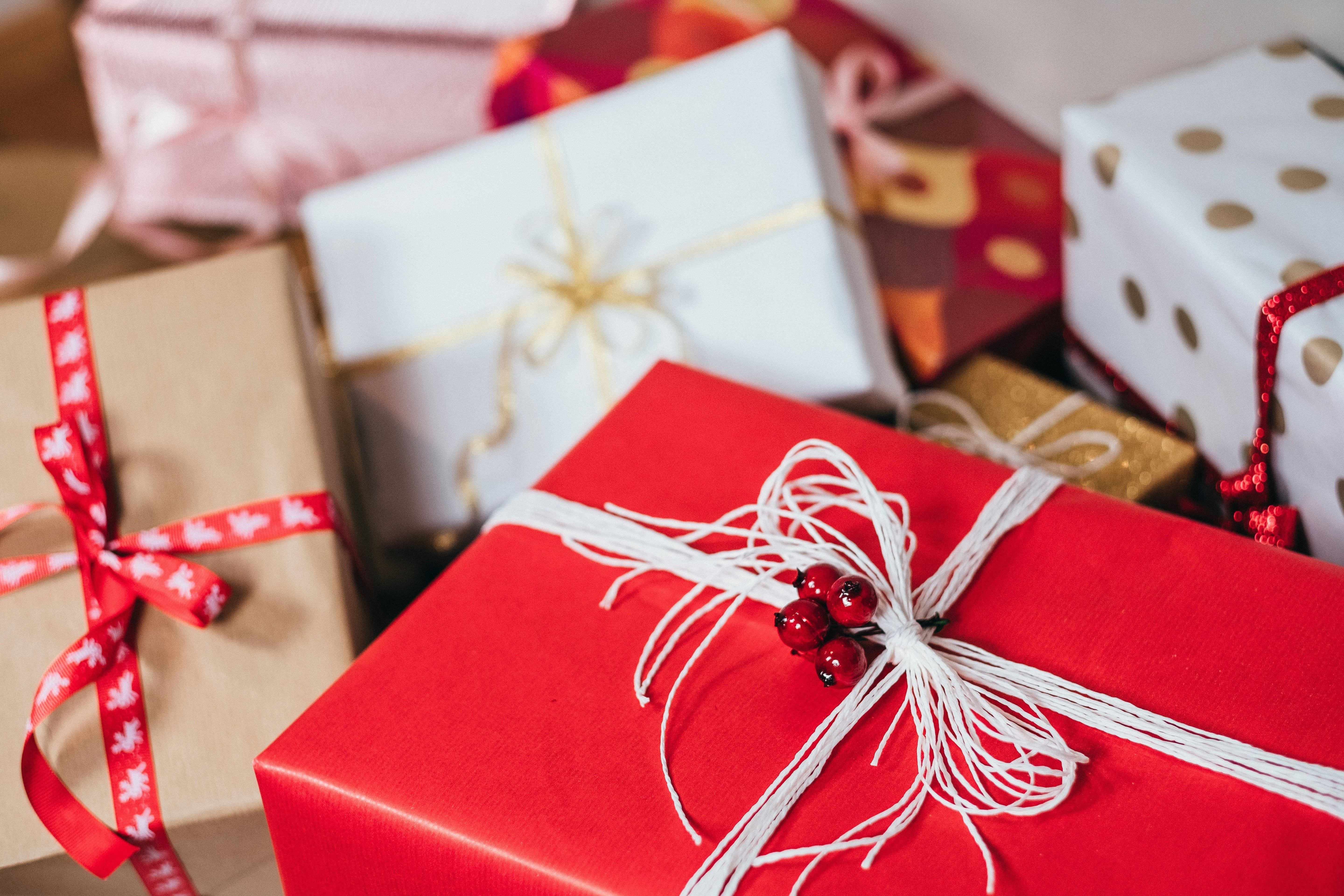 A festive arrangement of wrapped Christmas gifts in various sizes and colors, including red, white, and gold boxes tied with decorative ribbons. The image conveys a holiday theme, suitable for promoting seasonal baby gift sets.