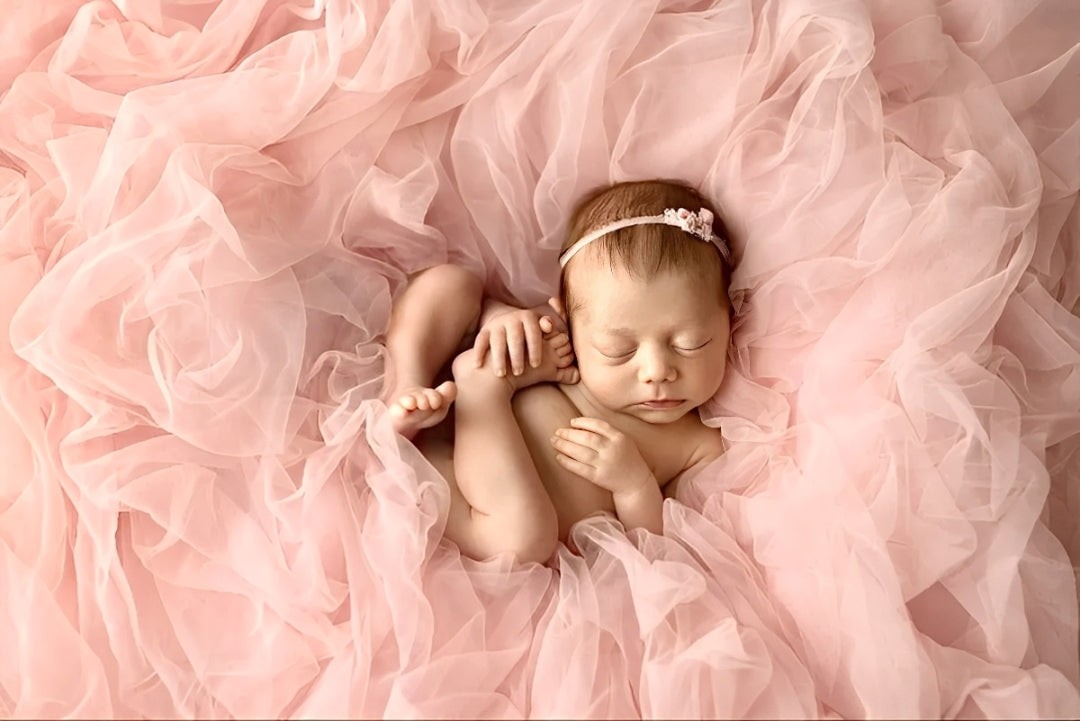 Newborn baby girl sleeping on pink tulle fabric, adorable gift bundle and personalized keepsake idea.