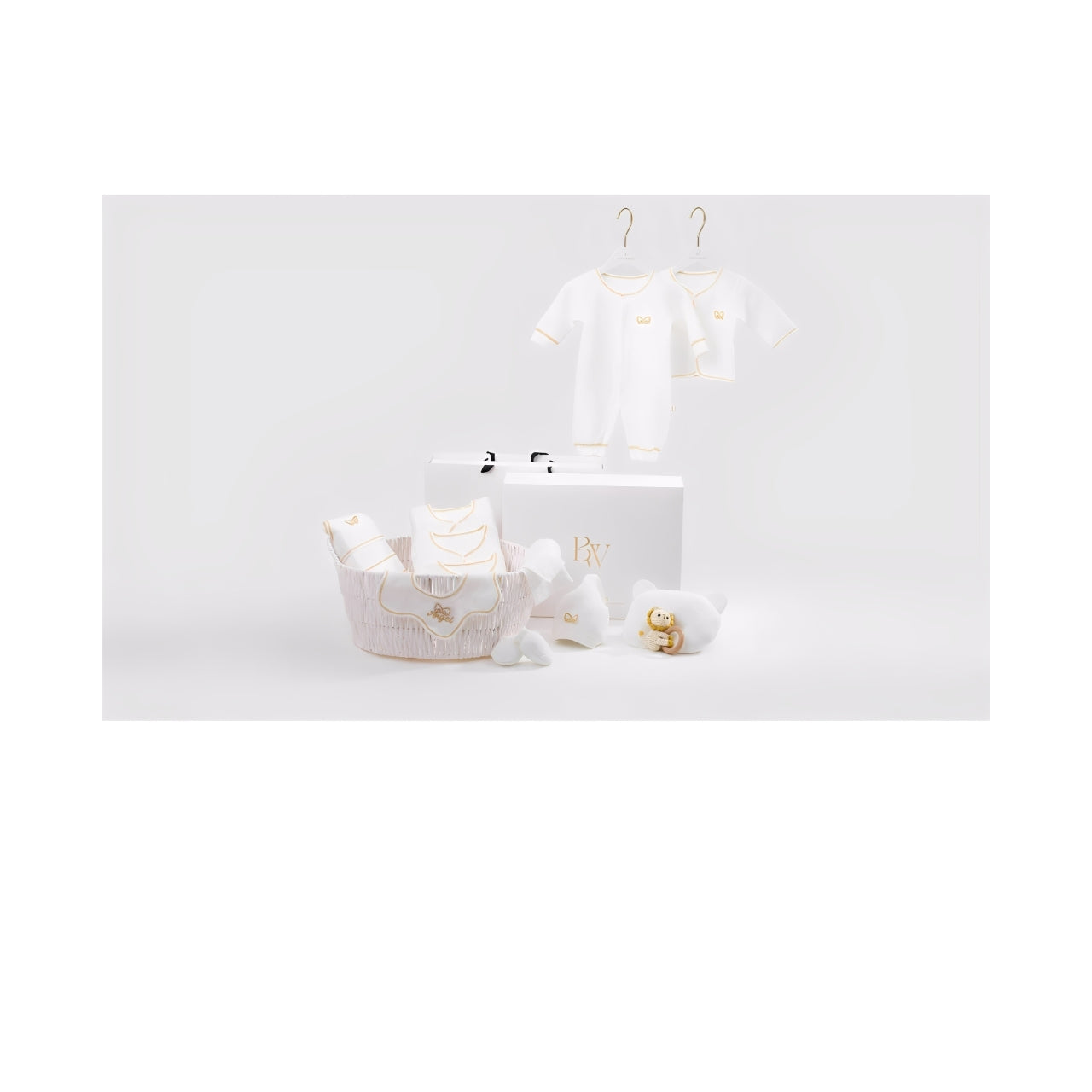 A luxury baby gift set featuring neatly arranged white essentials including clothing, plush toys, and accessories, placed in a soft fabric basket with a premium gift box in the background.