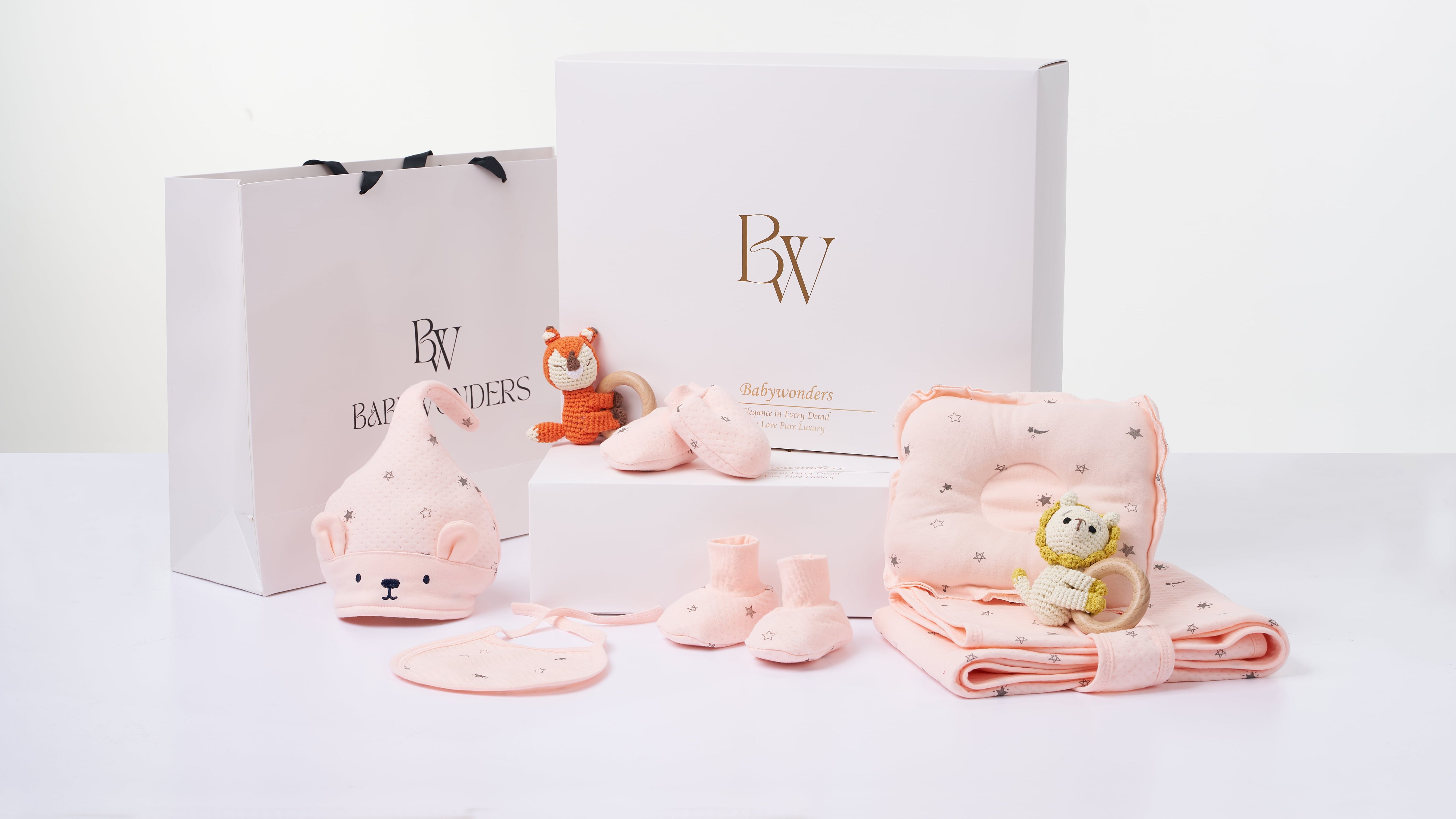 Developmental baby gift set in soft pink hues, with sensory-friendly items like plush animals, baby booties, and a muslin wrap—ideal for supporting early milestones.