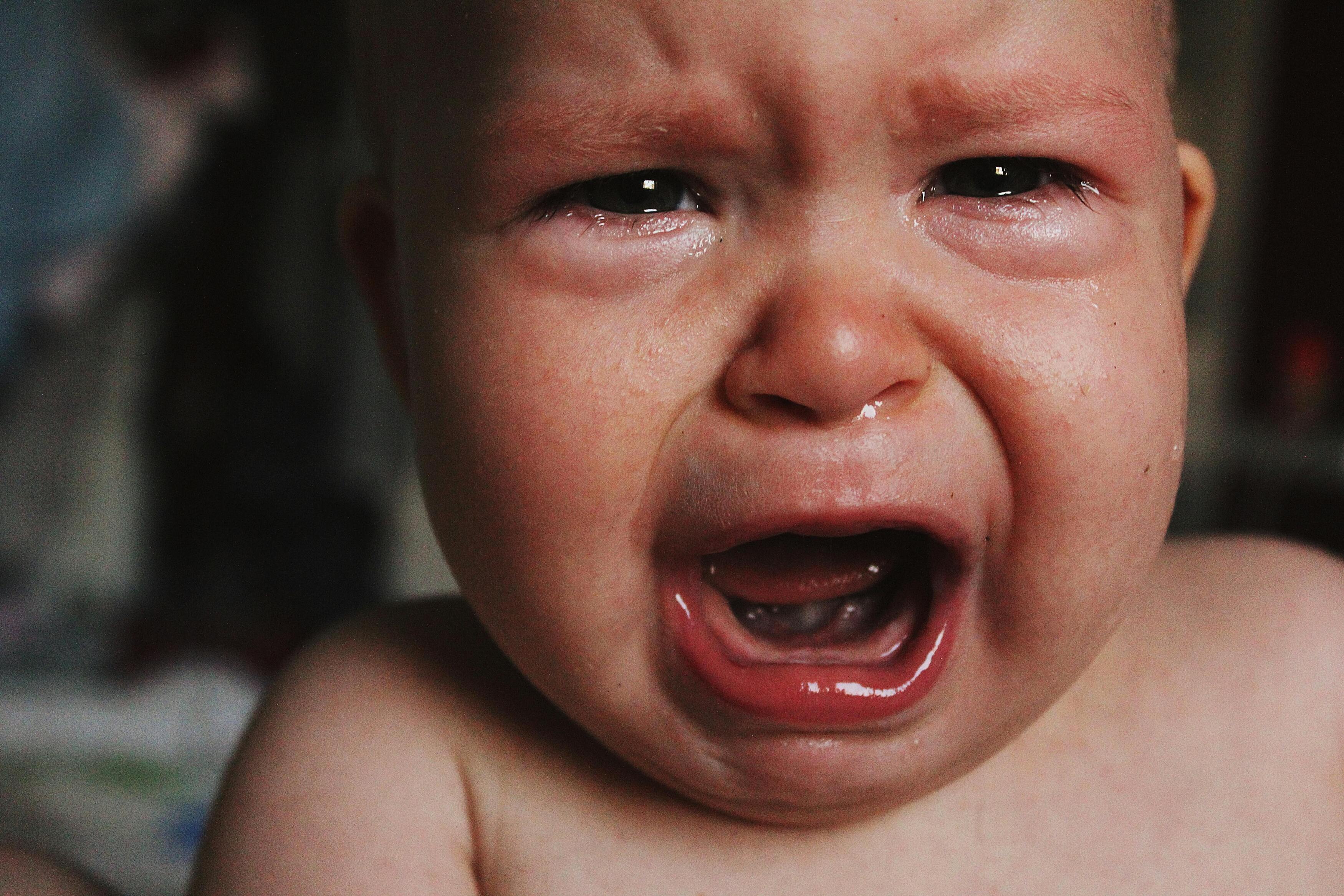 Close-up of a distressed crying baby with teary eyes and open mouth, seeking comfort.