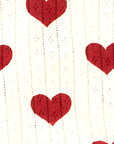 Detailed close-up of cream ribbed cotton fabric featuring red heart pattern, showing soft breathable knit texture.