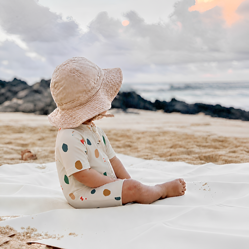 Toddler wearing abstract print zip swim romper sitting on beach, lightweight stretchy baby summer swimsuit for outdoor play