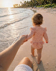 baby girl wearing pink confetti dot long sleeve swimsuit at the beach
