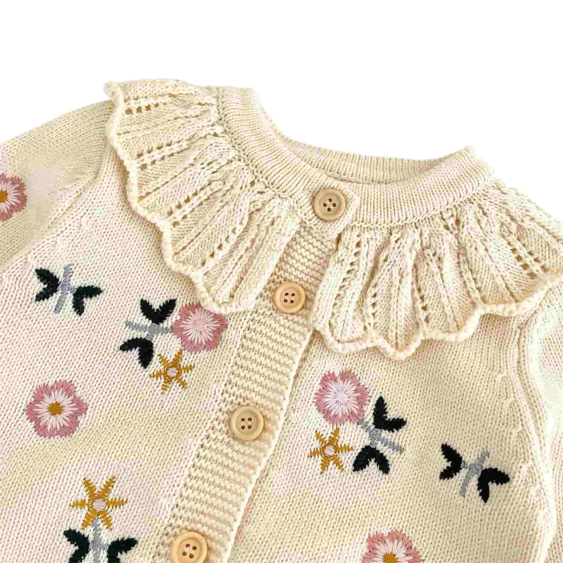 Close-up of baby floral knit cardigan in apricot showing ruffle collar and delicate embroidered flower details
