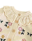 Close-up of baby floral knit cardigan in apricot showing ruffle collar and delicate embroidered flower details
