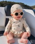 baby girl wearing beige floral long sleeve swimsuit with matching swim hat and sunglasses