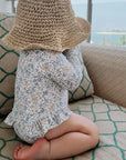 Baby wearing beige floral long sleeve swimsuit sitting indoors with straw hat, soft breathable toddler swimwear