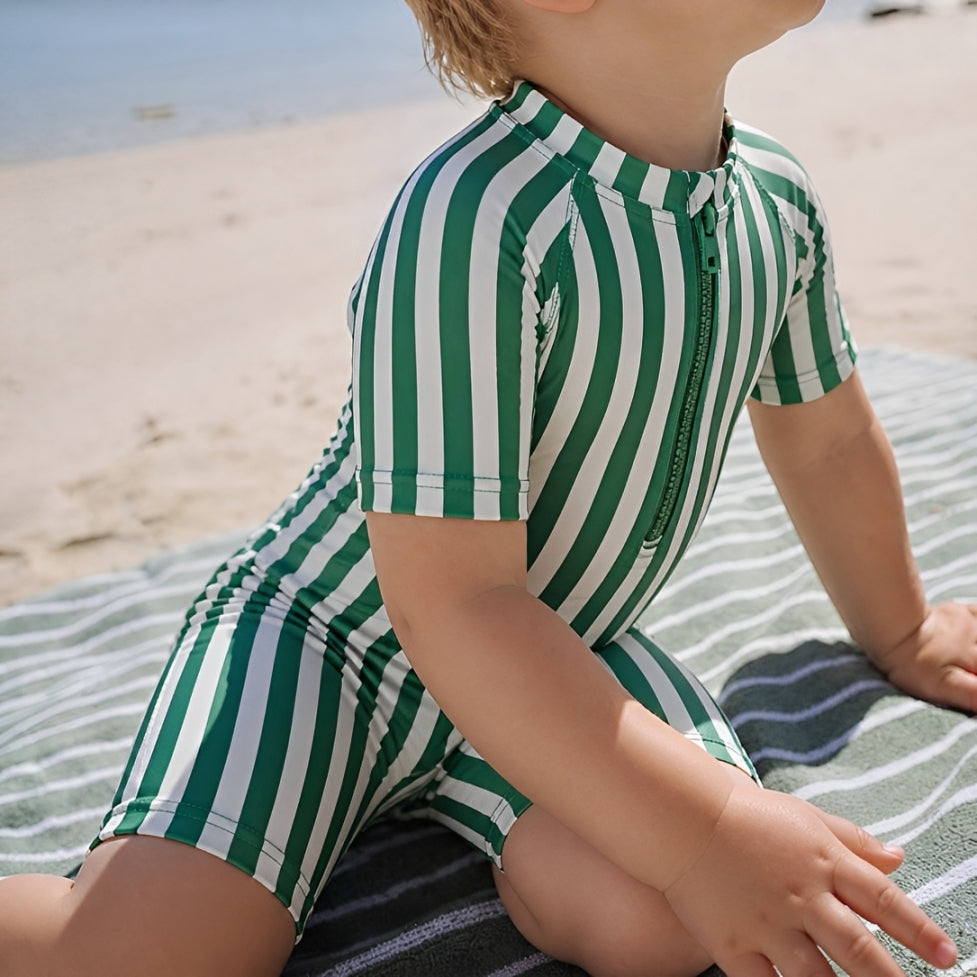 Baby wearing green stripe short sleeve zip swim romper sitting on beach towel, lightweight breathable summer baby swimwear

