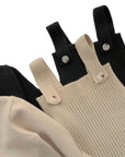 Detail of baby knitted overalls in beige and black showing button straps and ribbed knit texture