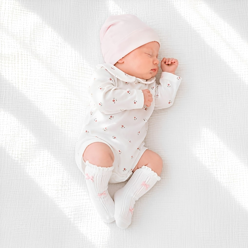 Baby wearing Peter Pan collar floral romper with white knit bow knee-high baby socks in soft neutral nursery setting