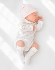 Baby wearing Peter Pan collar floral romper with white knit bow knee-high baby socks in soft neutral nursery setting