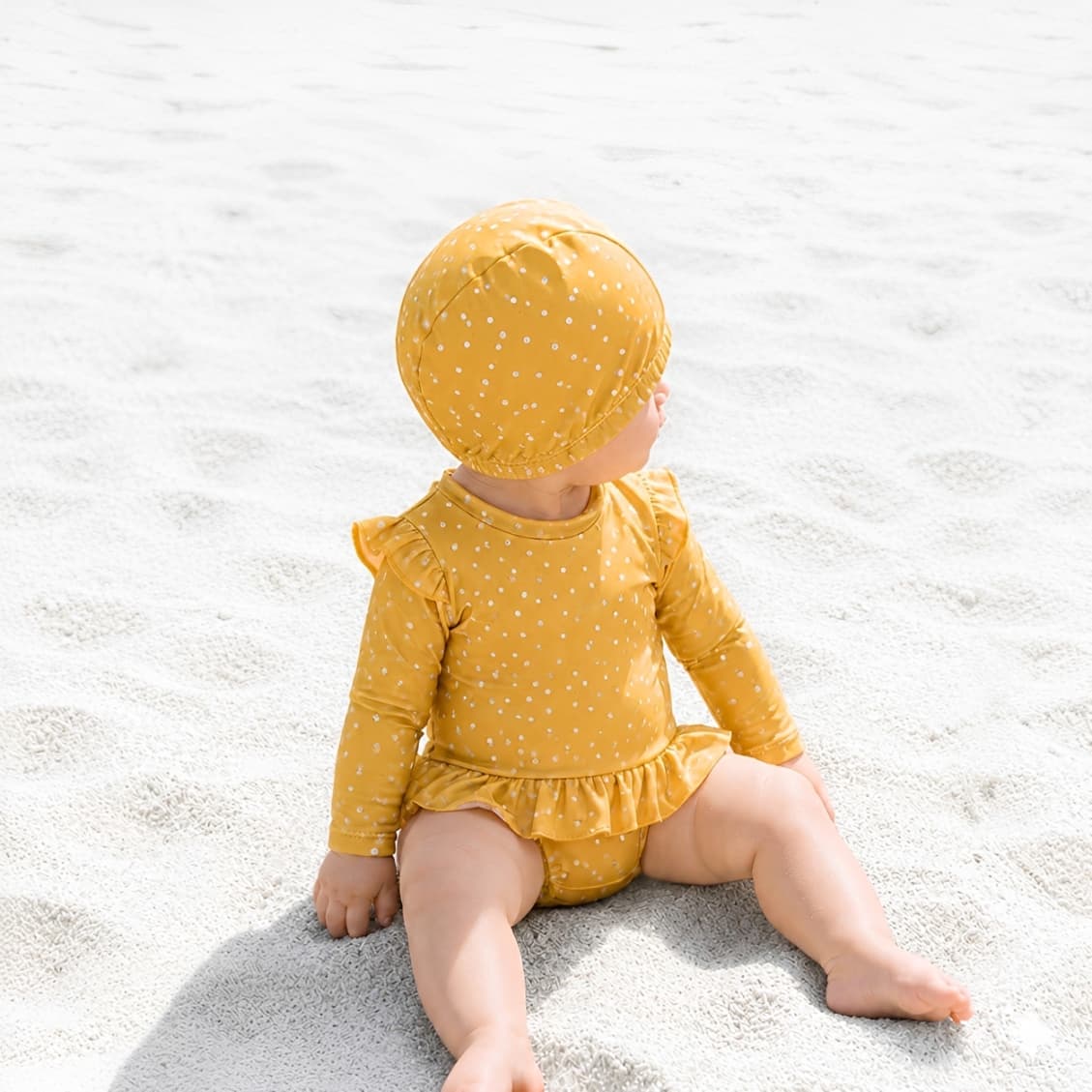 Baby in yellow polka dot long sleeve swimsuit sitting on beach sand, lightweight breathable toddler swimwear for summer