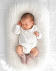Baby wearing white polka dot Peter Pan collar romper with blush pink frill lace baby socks lying on soft neutral baby nest bedding