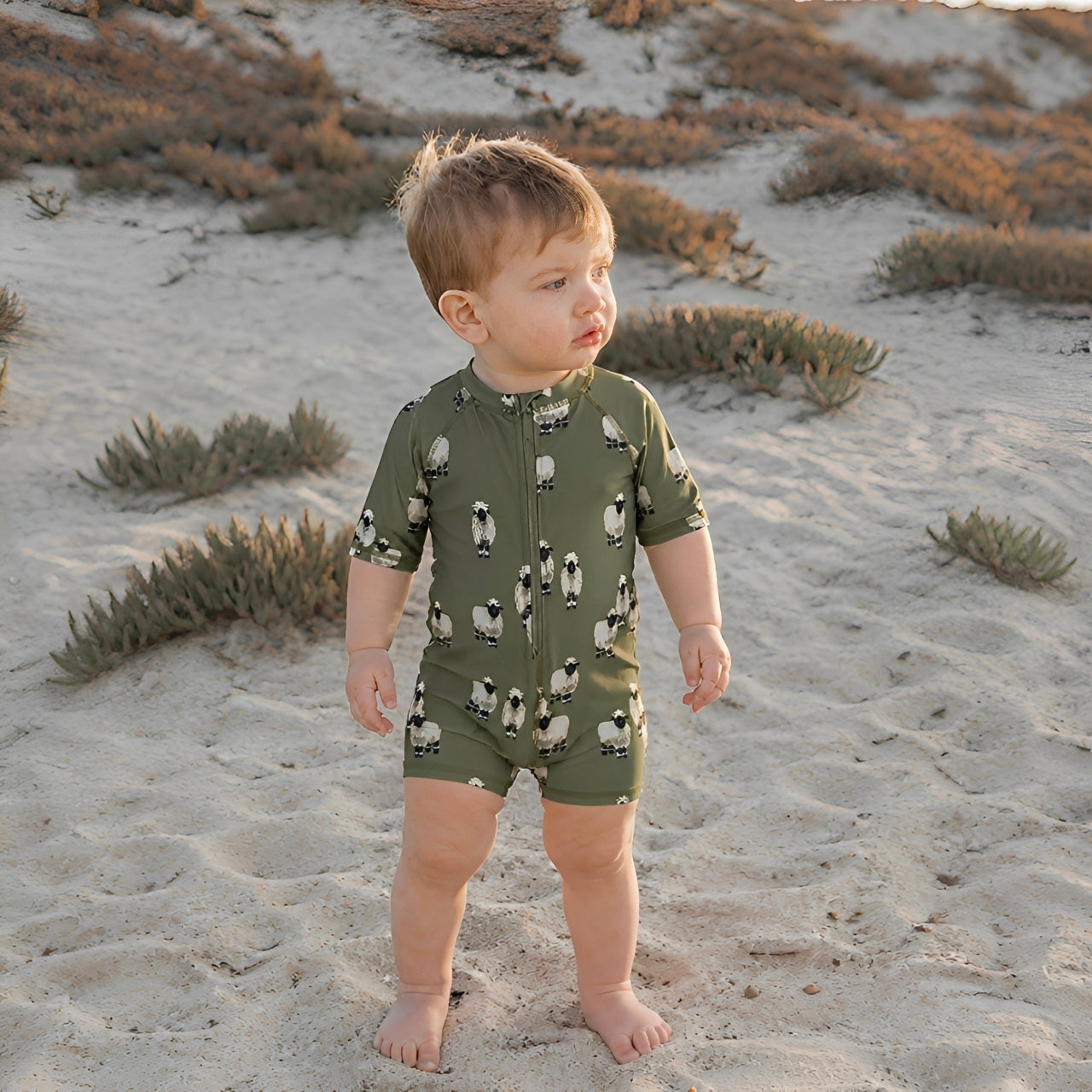 Toddler wearing green sheep print zip swim romper on the beach, soft breathable baby swimwear for summer play