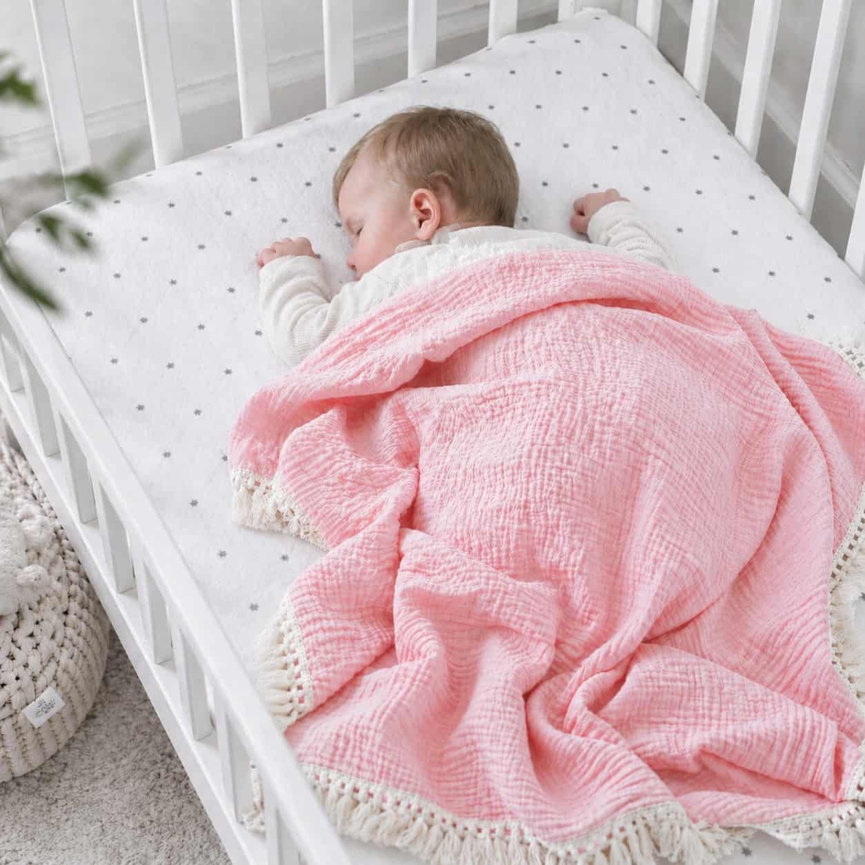 Sleeping newborn baby covered with a pink cotton baby blanket in a cot, soft breathable blanket for nursery and everyday comfort.