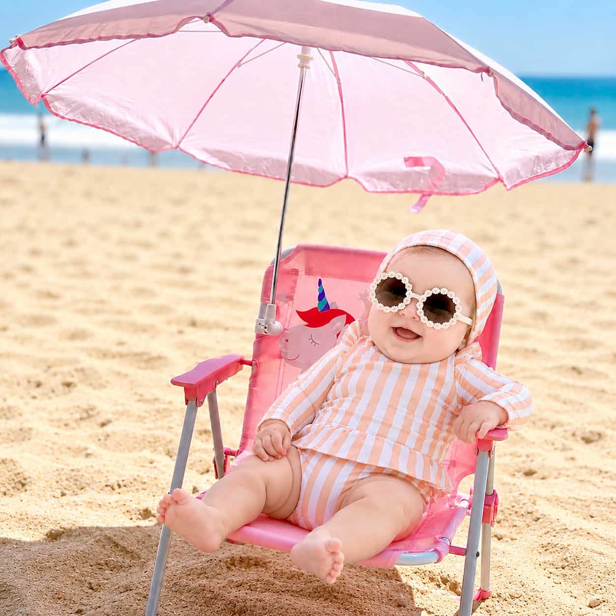 baby girl wearing pink striped long sleeve swimsuit with matching swim hat and sunglasses