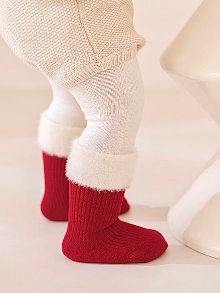 Baby wearing red Christmas socks with soft white cuffs, festive and warm winter look.