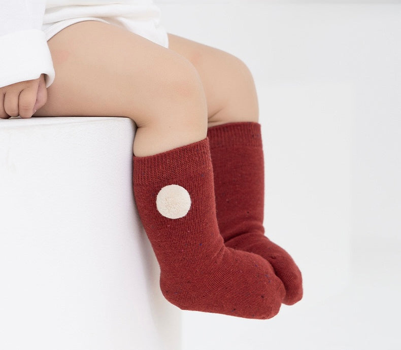Baby wearing red cotton socks with white pom pom accent, cozy and soft for Christmas season.
